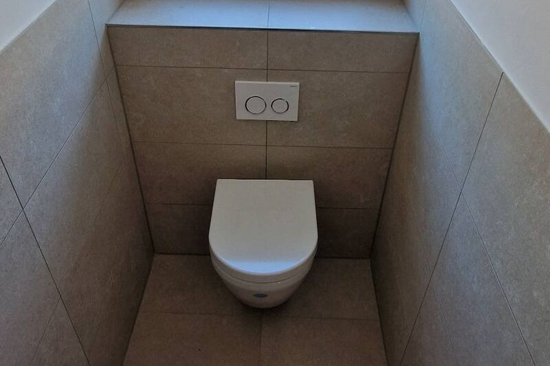 Nachher: Gäste-WC mit Wand-WC, halbhoch gefliesten Wänden in Steinoptik und gefliester Fensterbank