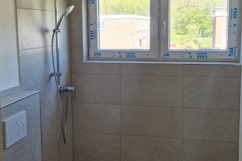 Nachher: Blick durch die Tür auf Dusche, Wand-WC und halbhoch geflieste Wände in Sandbeige