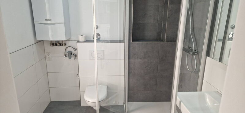 Nachher: Dusche mit Glasabtrennung und anthrazitfarbenen Fliesen, Ablagenische, Wand-WC und weiße Großformatfliesen