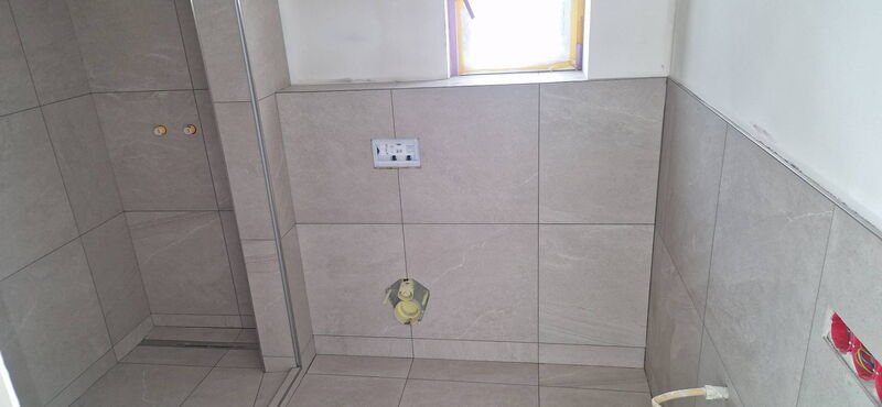 Nachher: großformatige Fliesen in heller Steinoptik, Vorwand mit Anschlüssen für das Wand-WC, Edelstahlprofil an der Kante