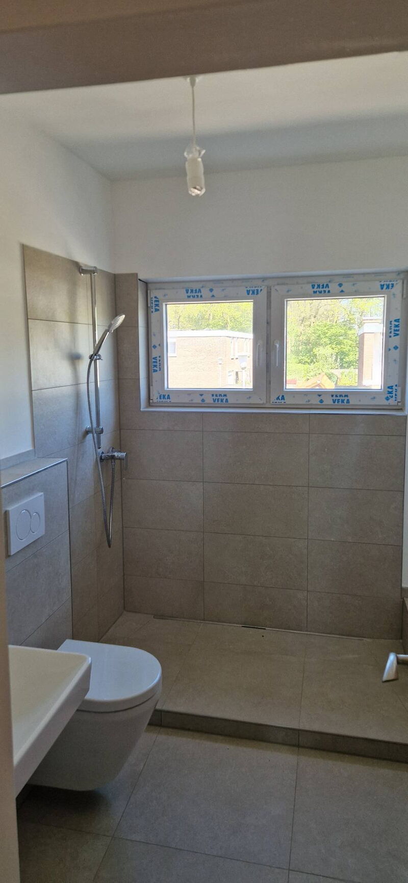 Nachher: Blick durch die Tür auf Dusche, Wand-WC und halbhoch geflieste Wände in Sandbeige