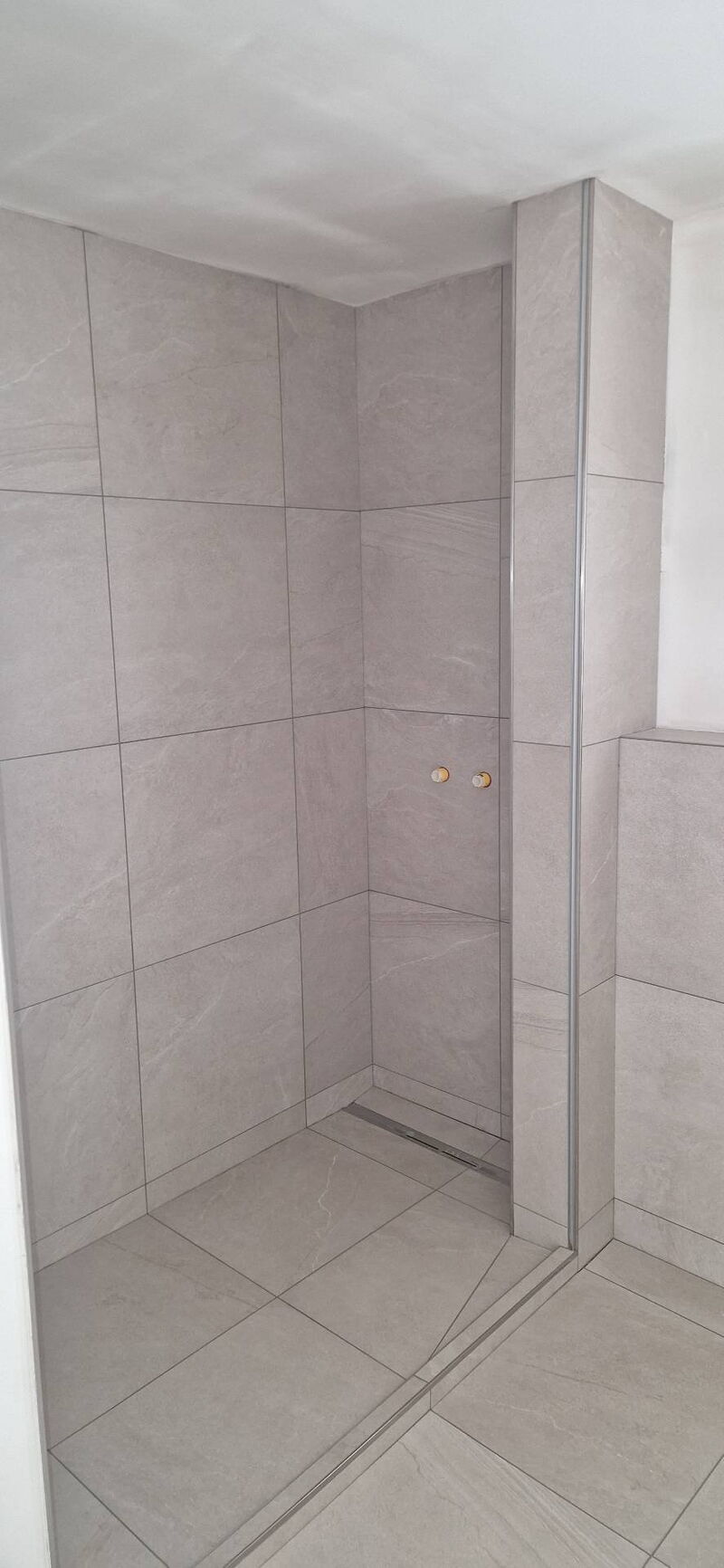 Nachher: bodengleiche Dusche mit Duschrinne, raumhoch gefliest in heller Steinoptik